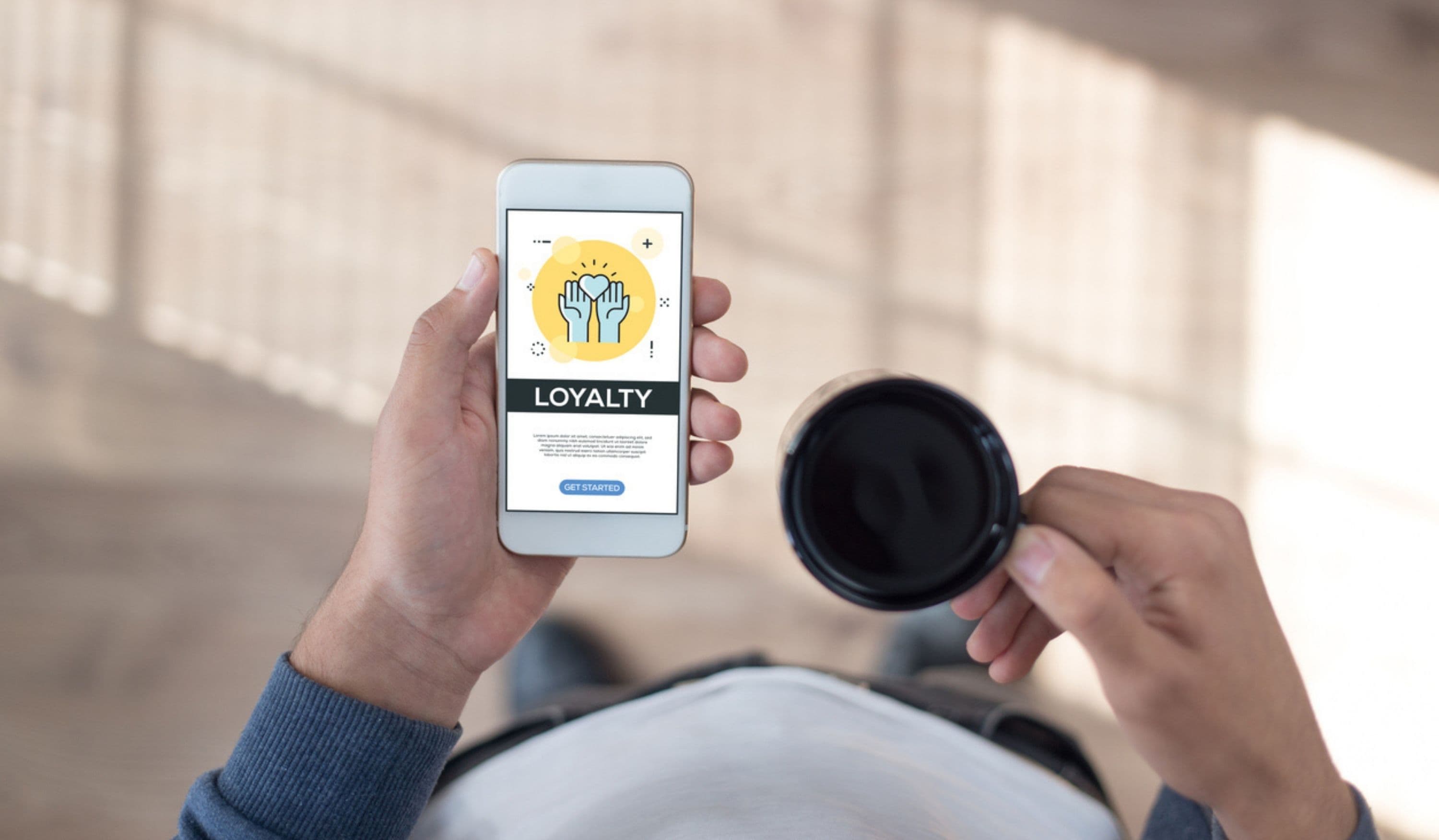 Person nutzt Kundenbindungs-App auf Smartphone mit Kaffeetasse in der Hand